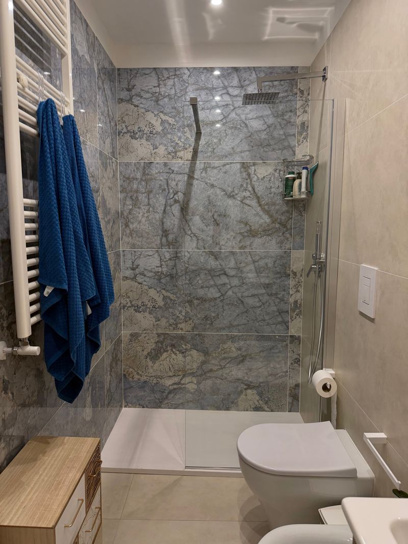 Bathroom with a shower clad in grey-blue marble and blue towels