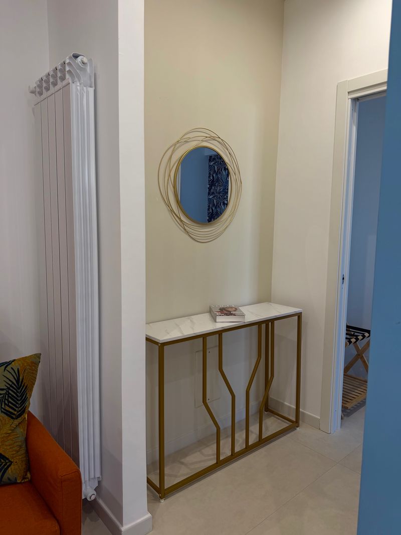 Hallway between the living room and bedroom, with a gold console table, round mirror and designer radiator