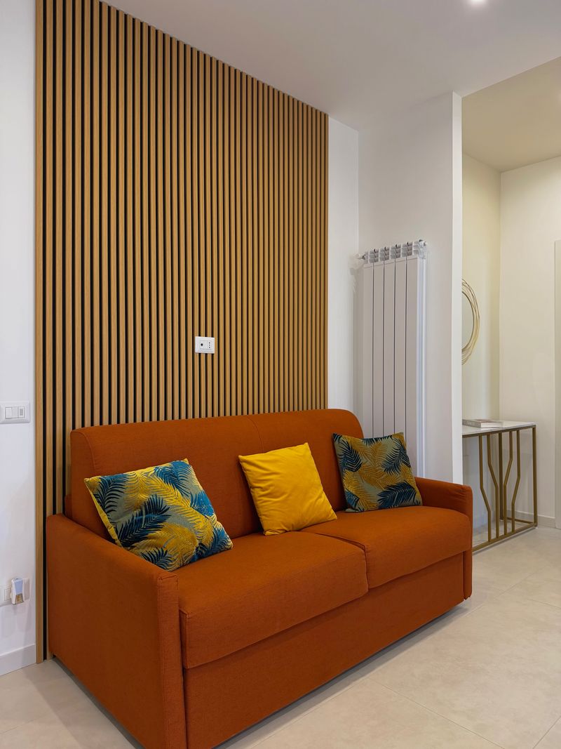 Orange sofa bed with yellow cushions in front of a wooden slat wall