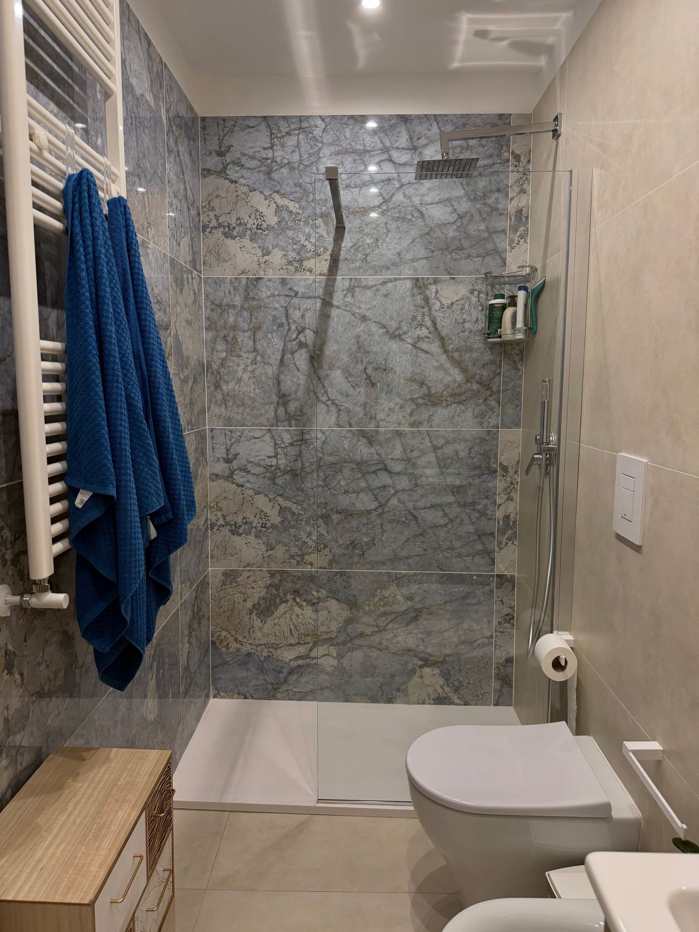 Bathroom with a shower clad in grey-blue marble and blue towels
