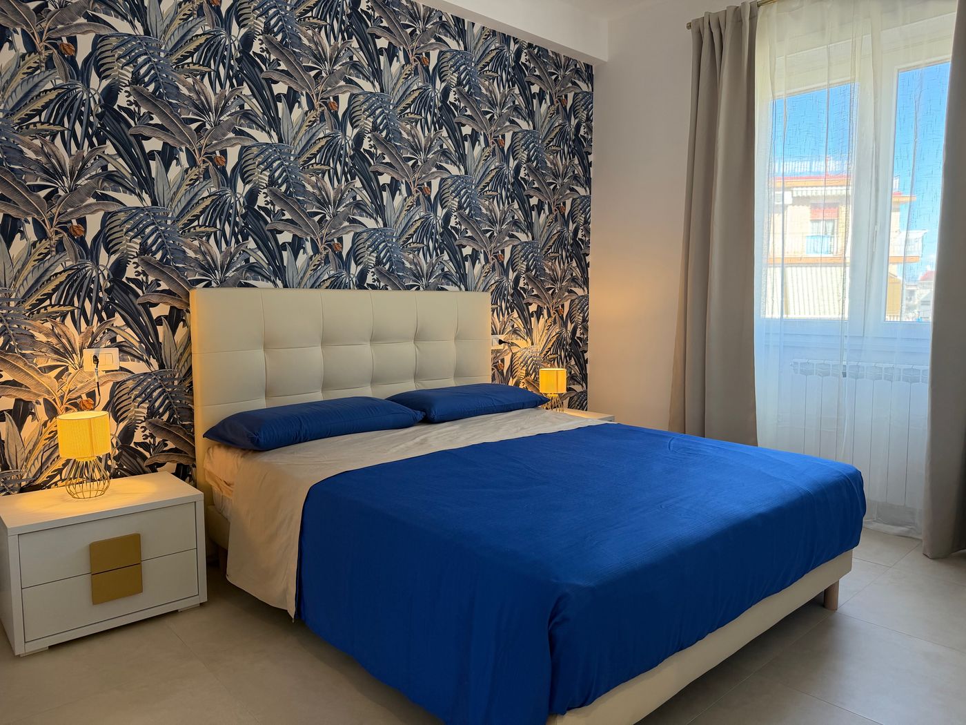 Double bedroom with blue leaf wallpaper, a padded headboard and a blue bedspread