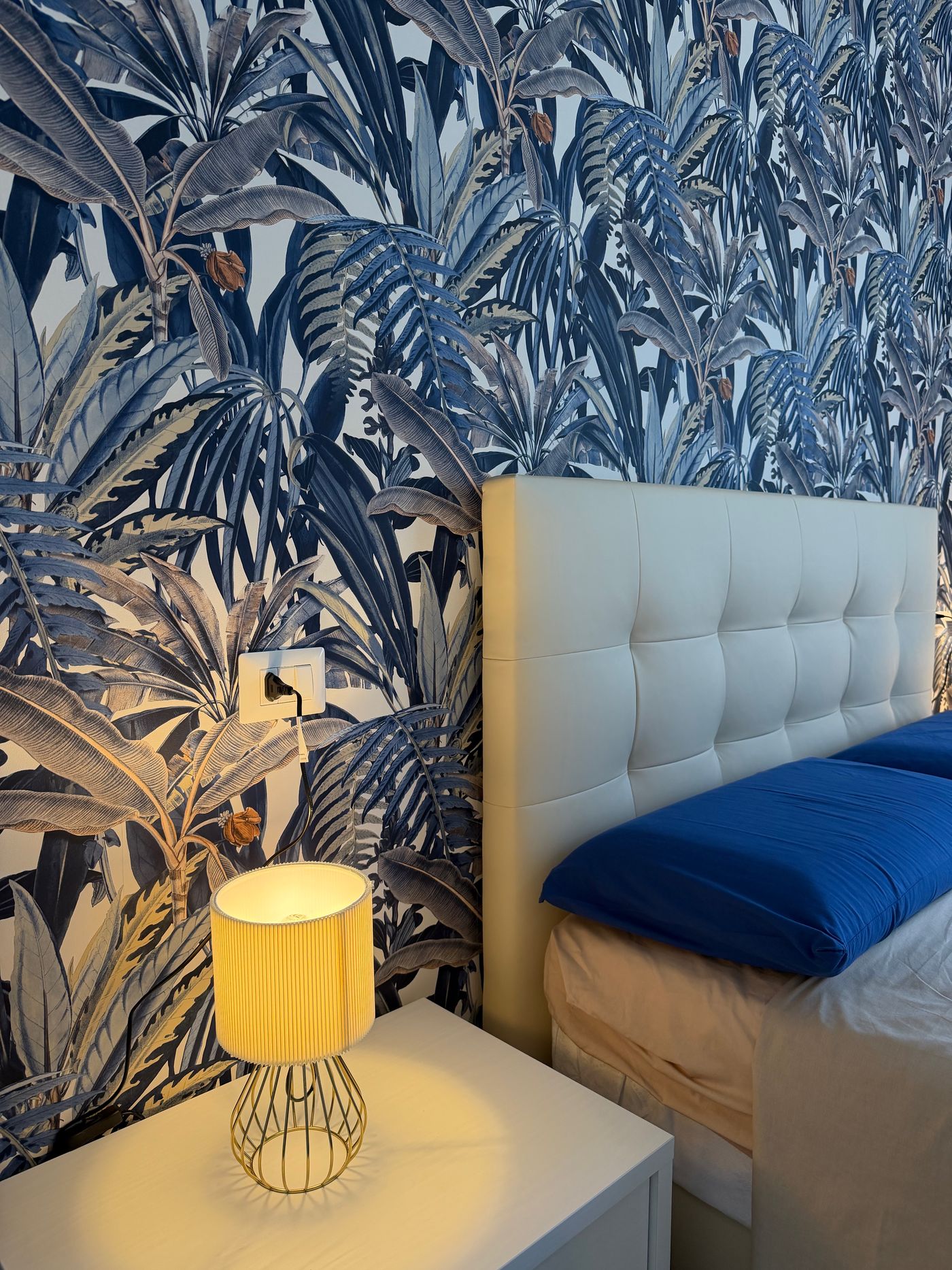 Bedside lamp glowing against the blue leaf wallpaper