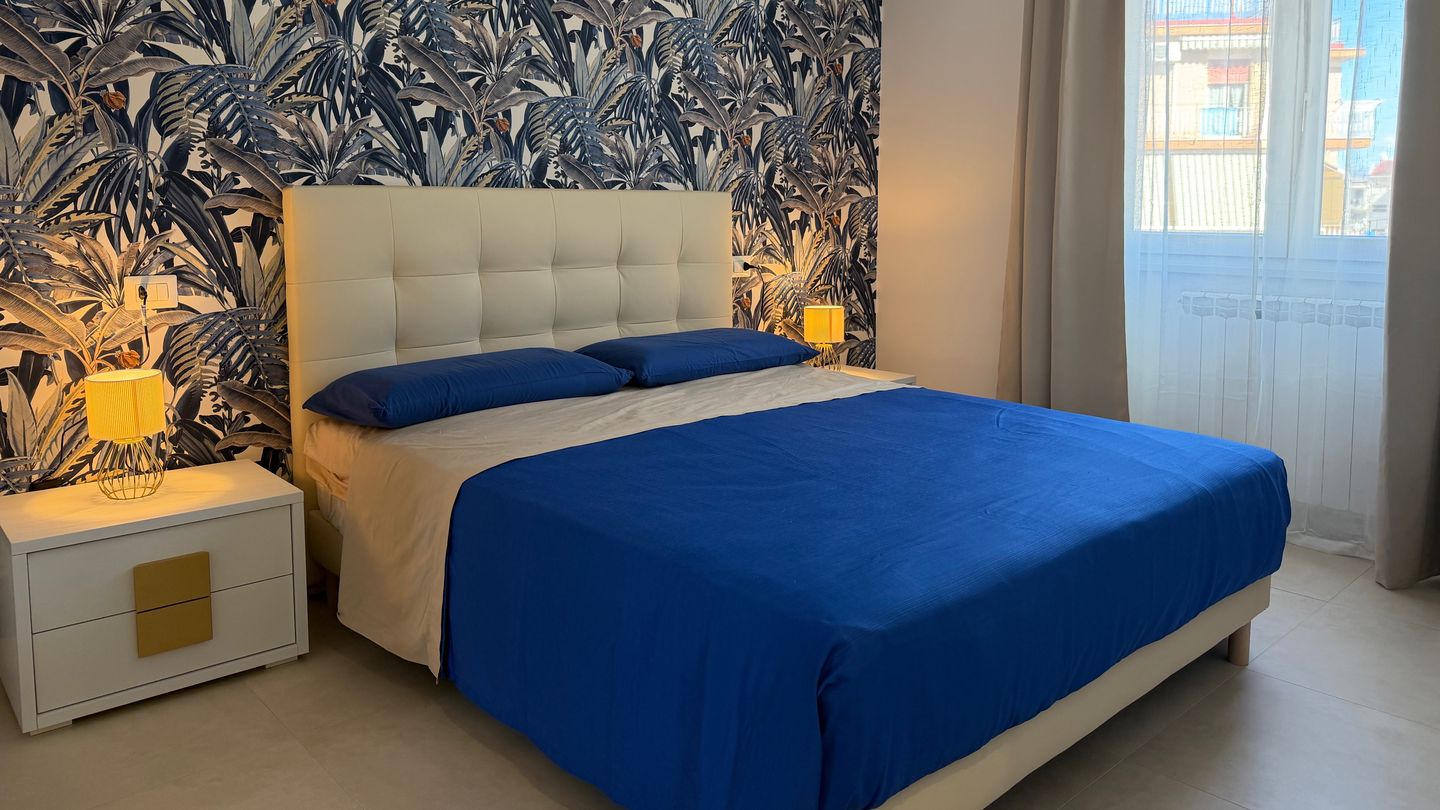 The double bedroom at Monì Boutique, with blue leaf wallpaper, a padded headboard and a blue bedspread