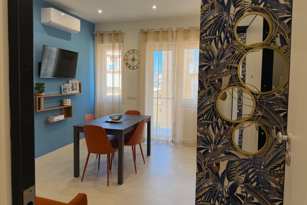 Living room with a light blue wall, dining table and terracotta chairs, seen from the entrance